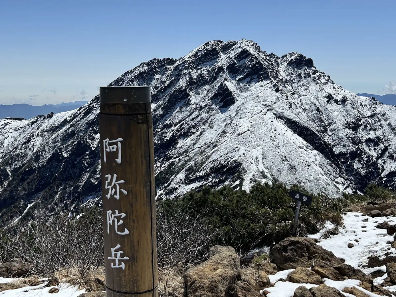 2026年5月15日の阿弥陀岳山頂付近。標識の奥に残雪の山肌が見える